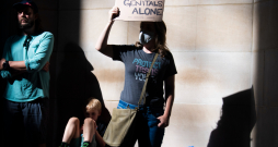 Protestētājs ar plakātu "Lieciet mierā mūsu ģenitālijas". 