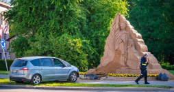 Sabojāta smilšu skulptūras apakšējā daļa, bet automobilim sabojāts priekšējais buferis un dzinēja pārsega sāni.
