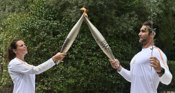Slavenā franču peldētāja Lora Manadū saņem olimpisko uguni no cita olimpisko spēļu čempiona grieķa Stefana Ntuskosa.