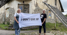Ieva un Dainis Grozas pie Lēdurgas kroga ieejas ar plakātu, kura teksts angļu valodā vēsta “Es nepadošos”. Esot aizgūts no mākslinieka Kristiana Brektes oriģināla.