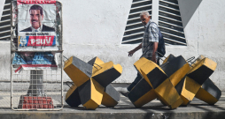 Vīrietis iet garām Venecuēlas prezidenta Nikolasa Maduro plakātam un prettanku barjerai Karakasā, 2025. gada 28. oktobrī. ASV spēki nogalināja 14 cilvēkus triecienos, kas iznīcināja četras, kā tiek apgalvots, narkotiku kontrabandā iesaistītas laivas Klusā okeāna austrumu daļā, otrdien paziņoja aizsardzības ministrs Pīts Hegsets.