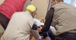 Kliente no auto līdz mājas durvīm tika atvesta ar transportēšanas gultu. Taču viņu neieveda mājās ar gultu vai ratiņkrēslā, bet nesa pa betona pakāpieniem, aiz segas stūriem turēdami. Istabā uzņemtajā attēlā apguldīšanas brīdis. Redzams, ka nav ne transportēšanas gultas, ne ratiņkrēsla. Citās reizēs mājās tika braukts gan ar gultu, gan ratiņkrēslu.