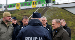 Polijas premjers Donalds Tusks (priekšā no labās) pirmdien sliežu spridzināšanas vietā pie Mikas stacijas. Tusks notikušo raksturoja kā bezprecedenta gadījumu, kas nozīmē "zināmu līniju" pārkāpšanu.