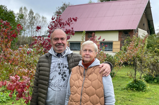 Aija Dzintra un Dainis Paukšēni 20 gados spējuši iekopt bagātīgu
ogulāju dārzu, kurā aug un ražo arī neparastāki augi. Attēlā: saimnieki savā dārzā, aiz muguras redzama māja, kurā ierīkota telpa ekskursantu grupu uzņemšanai.