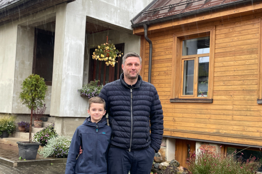 Saimnieks Ivars Grantiņš ar dēlu Ernestu mājas pagalmā, kur labi redzams, kā senākā daļa savienota ar no jauna uzbūvēto nodegušā apjoma
vietā.