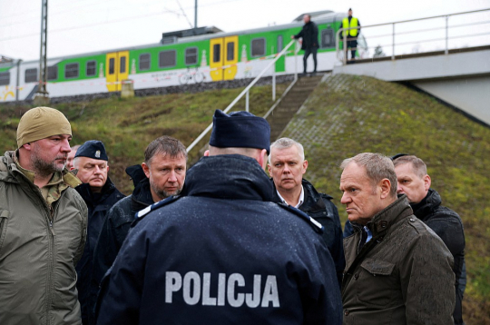 Polijas premjers Donalds Tusks (priekšā no labās) pirmdien sliežu spridzināšanas vietā pie Mikas stacijas. Tusks notikušo raksturoja kā bezprecedenta gadījumu, kas nozīmē "zināmu līniju" pārkāpšanu.