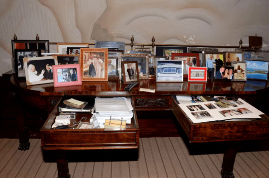 Epstīna faili. 
Fotogrāfijā redzams galds ar atvērtu atvilktni, kur atrodas kaudzīte ar fotogrāfijām, tai skaitā foto, kur Tramps ir kopā ar bikini tērptām sievietēm. Šis Trampa foto uzņemts pirms viņš kļuva par prezidentu.