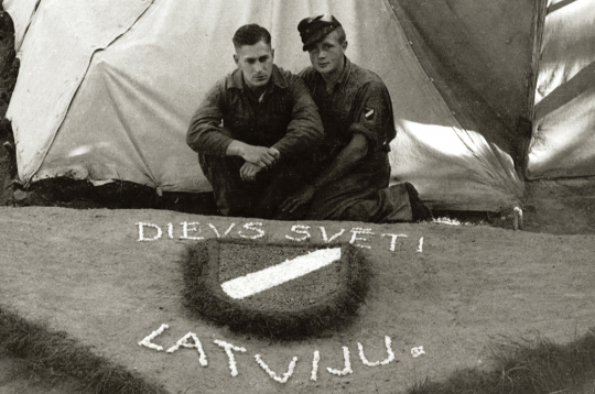 Internētie latviešu leģionāri pie pašdarināta rotājuma – latviešu leģiona vairodziņa. Ēkšes – Rennesletes nometne, 1945. gada
vasara.