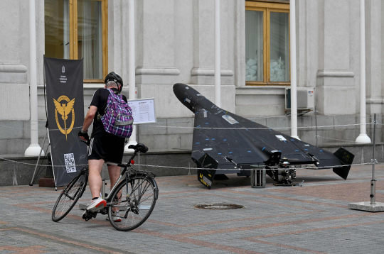 Vīrietis lasa informatīvu stendu pie Irānā ražota bezpilota lidaparāta Shahed 136 (Geranium-2), kas izstādīts pie Ukrainas Ārlietu ministrijas ēkas Kijivā 2025. gada 21. jūlijā Krievijas iebrukuma Ukrainā laikā.