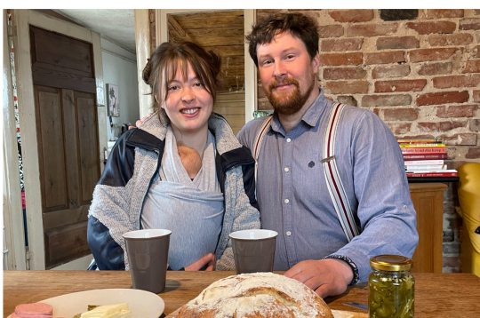 Ellena un Gunārs ar savu pirmdzimto lielajā istabā, kur uz brokastu galda
ir arī saimnieka cepta maize.