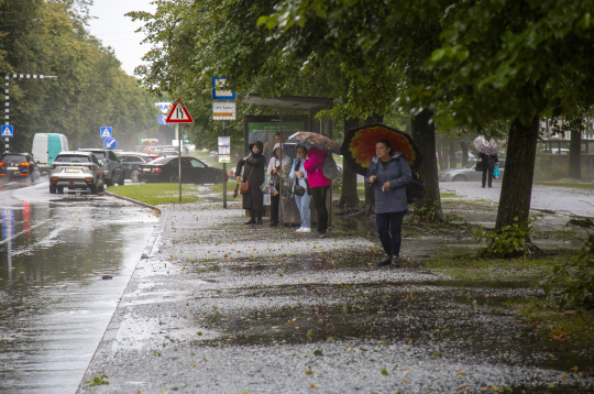 Cilvēki autobusa pieturā negaisa laikā Rīgā.