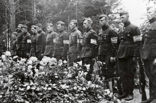 Bijušo Latvijas armijas karavīru un aizsargu – tobrīd Vācijas kārtības
dienesta darbinieku ierinda  pie padomju okupācijas Baigā gada
upuru masu kapa. 1941. gada vasara.