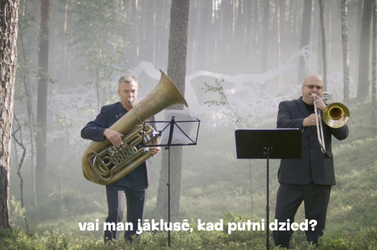 Ekrānuzņēmums no dziesmas "Kā?" videoklipa. Ekrānuzņēmums no dziesmas "Kā?" videoklipa.