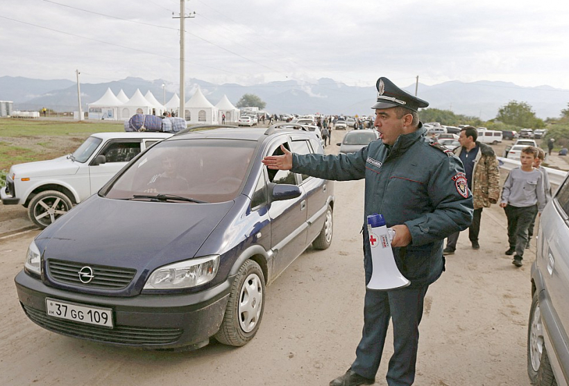 Armēņu policists regulē bēgļu ierašanos Kornidzorā, kas ir Armēnijas un Kalnu Karabahas robežciems. Tur viena pēc otras ierodas ļaužu un mantu pilnas automašīnas.