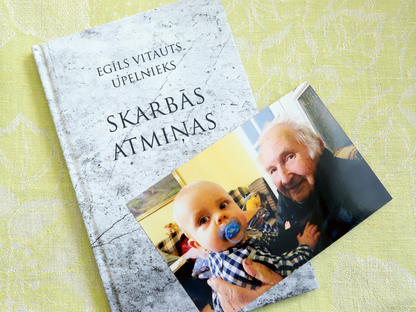 Laumas Upelnieces tēva dzejas grāmata, uz tās fotogrāfijā redzams autors Egīls Vitauts Upelnieks, Lāčplēša Kara ordeņa kavaliera kapteiņa Kristapa Kriša Upelnieka dēls, un mazmazdēls Juris.