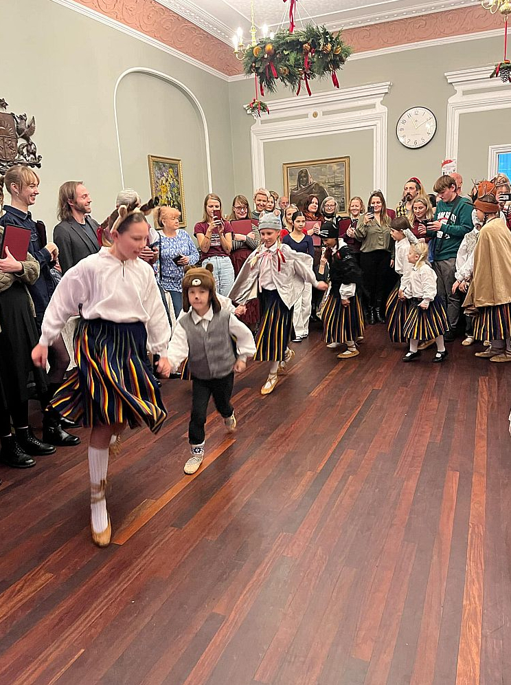 Bērnu tautas deju kopa "Vanadzēni" uzstājas Ziemassvētku tirdziņā Daugavas vanagu fonda Londonas namā, fonā – tirgotāji.