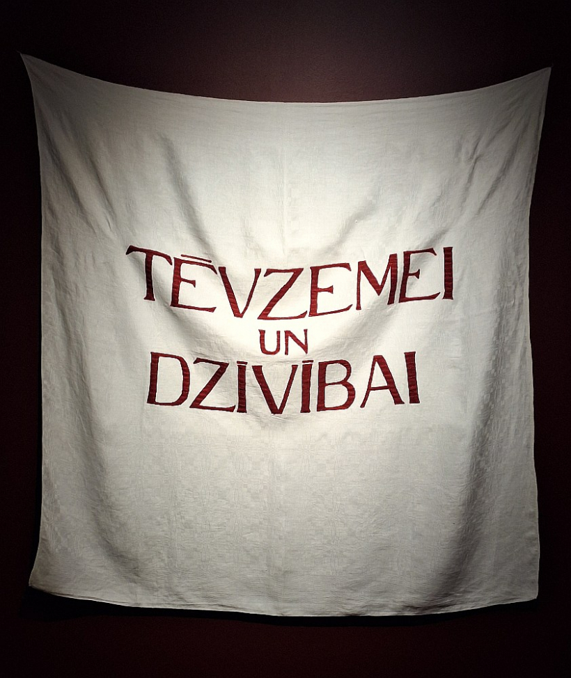 Laura Dzērve. "Tēvzemei un dzīvībai". 2025, tekstila aplikācija, 140 x 140 cm. Māksliniece teic: "Mēs vienmēr esam tiekušies pēc brīvības, bet vai protam dzīvot brīvā valstī? Vai, baudot šo brīvību, spējam izvēlēties atbildīgi?"