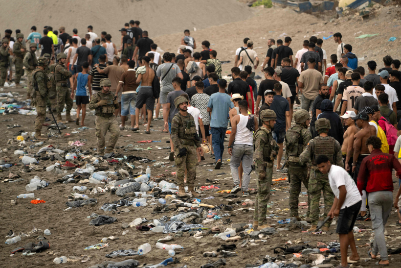 Pie žoga netālu no sadursmju vietas pie Fnidekas, uz Marokas un Spānijas robežas, 2026. gada 31. jūlijā pulcējušies cilvēki. Tūkstošiem migrantu nakts laikā no Marokas šķērsoja robežu un iekļuva Spānijas Ziemeļāfrikas anklāvā Seutā, 31. jūlijā pavēstīja policijas avots. 