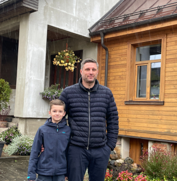 Saimnieks Ivars Grantiņš ar dēlu Ernestu mājas pagalmā, kur labi redzams, kā senākā daļa savienota ar no jauna uzbūvēto nodegušā apjoma
vietā.