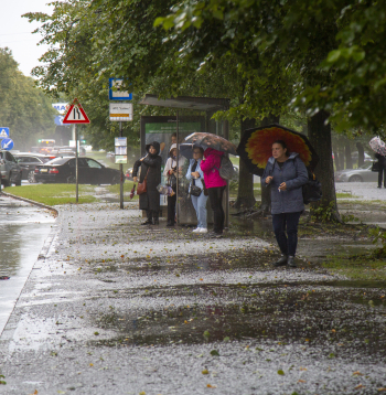 Cilvēki autobusa pieturā negaisa laikā Rīgā.