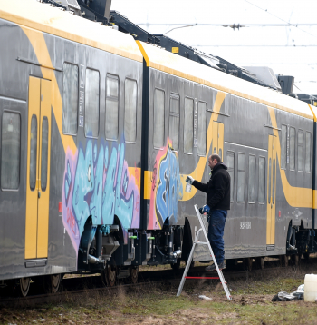 Vīrietis mazgā ar grafiti apķēpātu jauno "Škoda Vagonka" elektrovilcienu Vagonu depo.