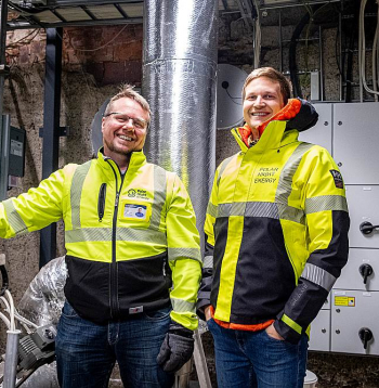 ""Polar Night Energy" valdes priekšsēdētājs Tommi Eronens (no labās puses) un pārstāvis Baltijas valstīs Petri Triggs (Trygg) demonstrē pirmo PNE izmēģinājuma smilšu bateriju. Vairāk kā 20 tonnas smilšu atrodas turpat aiz sienas.
