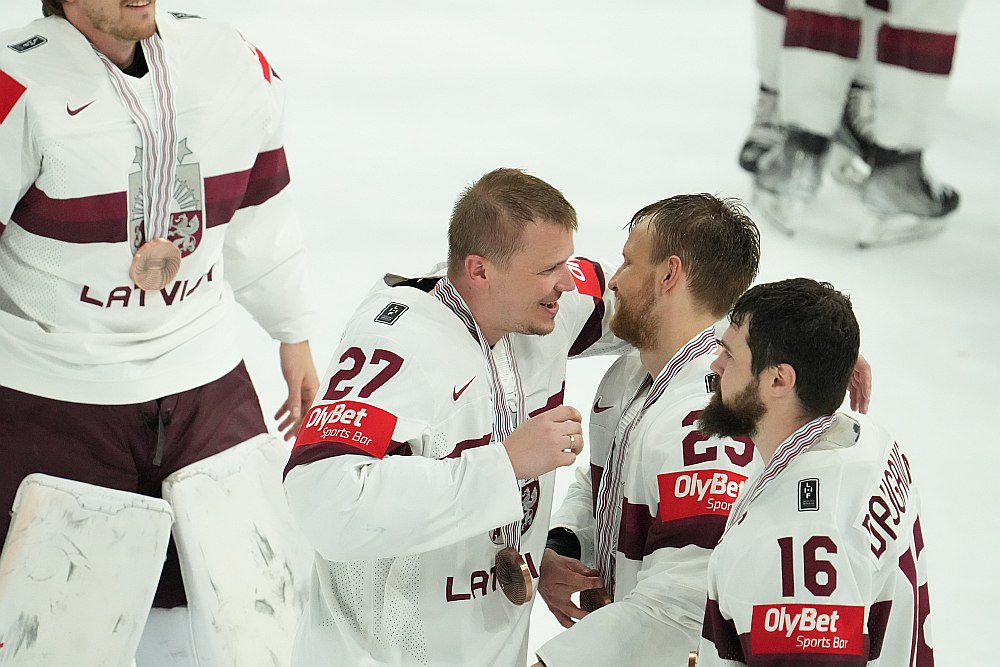 Latvijas hokeja izlases spēlētāji ar bronzas medaļām pēc pasaules hokeja čempionāta spēles starp Latvijas un ASV valstsvienībām ''Nokia arēnā'' Tamperē. Uz sporta krekla piedurknes skaidri saskatāma reklāma "Olybet Sporta bārs".