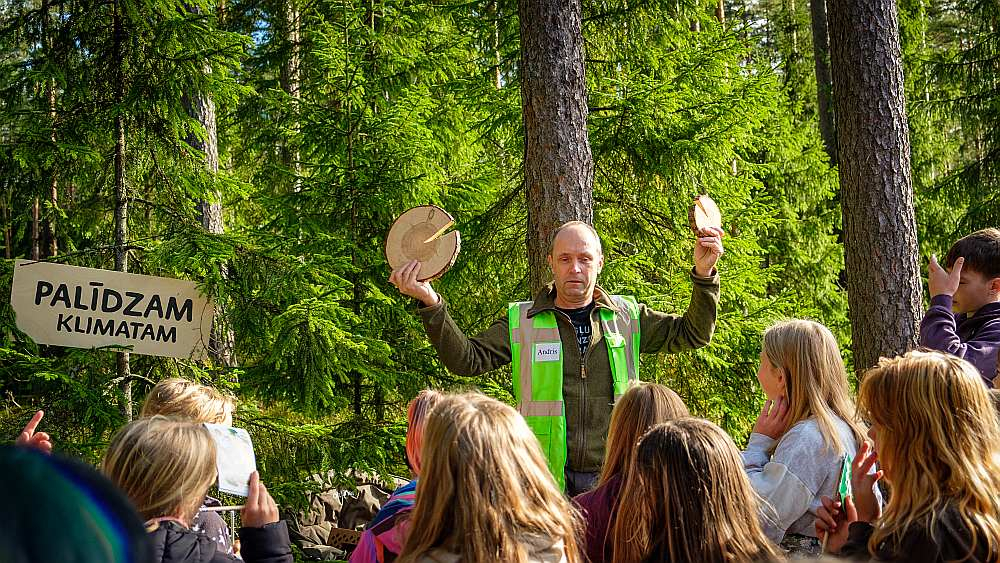 Daugmales skolēni ar interesi klausās LVM darbinieku stāstos par norisēm mežā.