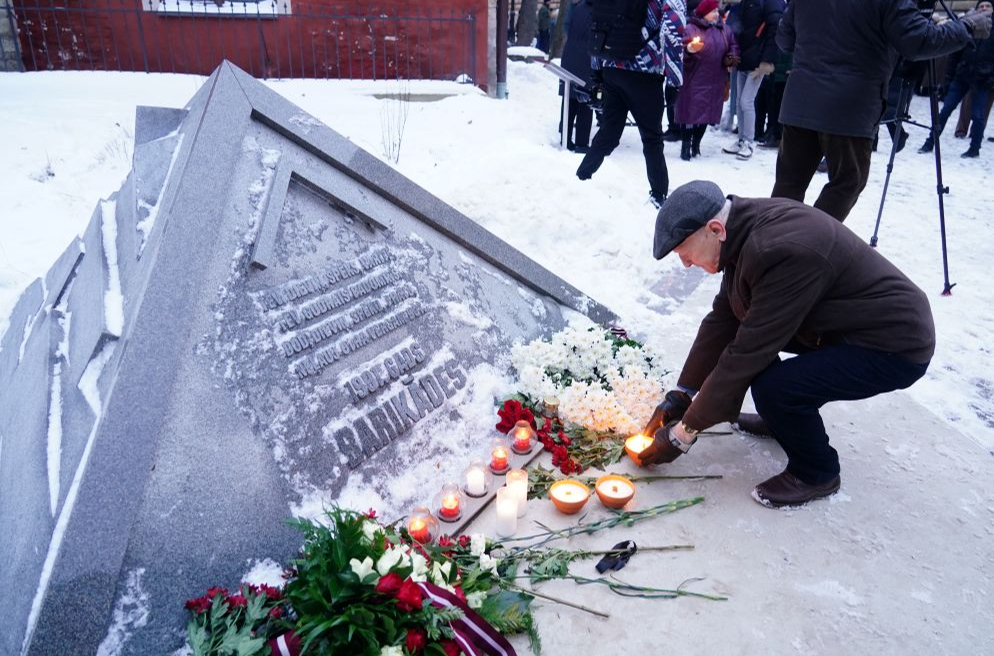 Cilvēki noliek sveces pie pieminekļa "1991. gada barikāžu piemiņas zīme" 1991. gada barikāžu atceres pasākuma laikā pie Saeimas nama.