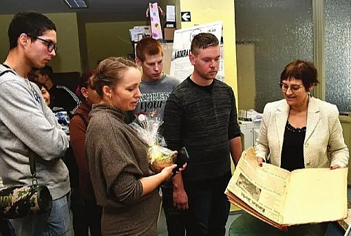 Avīzes galvenā redaktore Anita Rozentāle (no labās) biedrības "Cerību spārni" jauniešus iepazīstina ar vēsturiskiem laikraksta izdevumiem.