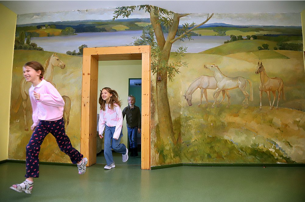 Vietējie iedzīvotāji priecājas par darba vietām, bet vienlaikus raizējas, vai arī viņu bērniem laukos būs perspektīvas. Attēlā: skolēni Bērzaunes pamatskolas centrālajā telpā ar Madonas novada leģendārā mākslinieka un sabiedriskā darbinieka Jāņa Simsona 1985. gadā veidoto sienas gleznojumu "Ainava ar zirgiem".