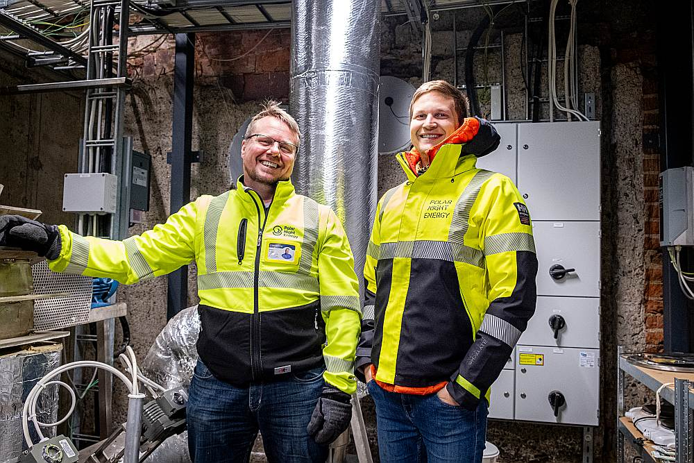 ""Polar Night Energy" valdes priekšsēdētājs Tommi Eronens (no labās puses) un pārstāvis Baltijas valstīs Petri Triggs (Trygg) demonstrē pirmo PNE izmēģinājuma smilšu bateriju. Vairāk kā 20 tonnas smilšu atrodas turpat aiz sienas.