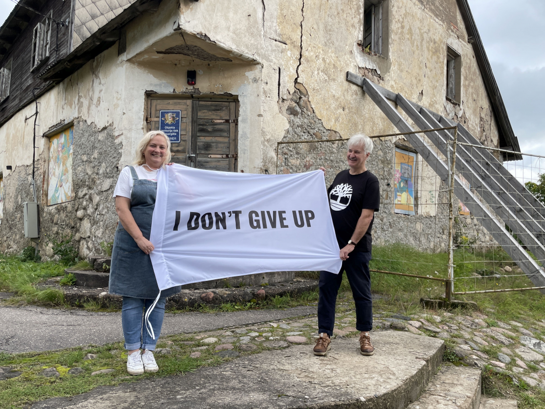 Ieva un Dainis Grozas pie Lēdurgas kroga ieejas ar plakātu, kura teksts angļu valodā vēsta “Es nepadošos”. Esot aizgūts no mākslinieka Kristiana Brektes oriģināla.