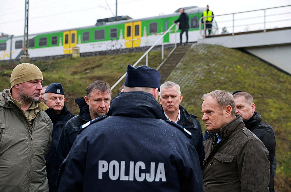 Polijas premjers Donalds Tusks (priekšā no labās) pirmdien sliežu spridzināšanas vietā pie Mikas stacijas. Tusks notikušo raksturoja kā bezprecedenta gadījumu, kas nozīmē "zināmu līniju" pārkāpšanu.