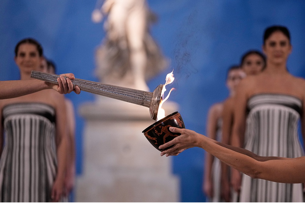 Milānas–Kortīnas olimpisko spēļu uguns tika iedegta, atkāpjoties no tradīcijām, jo bija bažas par nelabvēlīgiem laika apstākļiem.