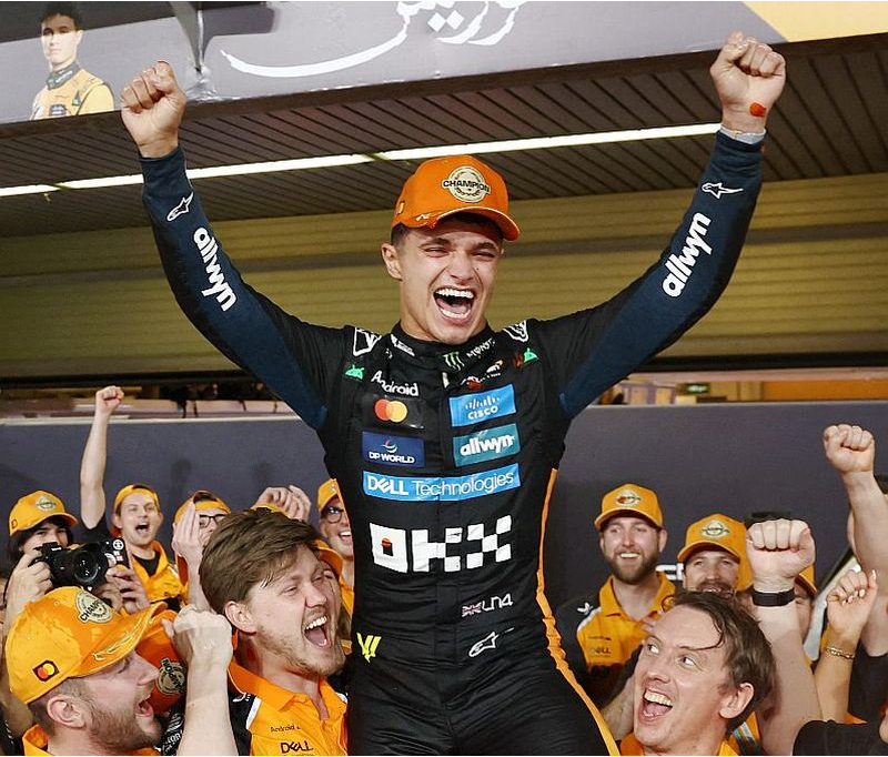 2025. gada F-1 čempions Lando Noriss uz "McLaren" komandas darbinieku pleciem. Noriss pirmo reizi kļuva par autosporta prestižāko sacensību uzvarētāju, no troņa gāžot iepriekšējo četru gadu uzvarētāju Maksu Verstapenu.