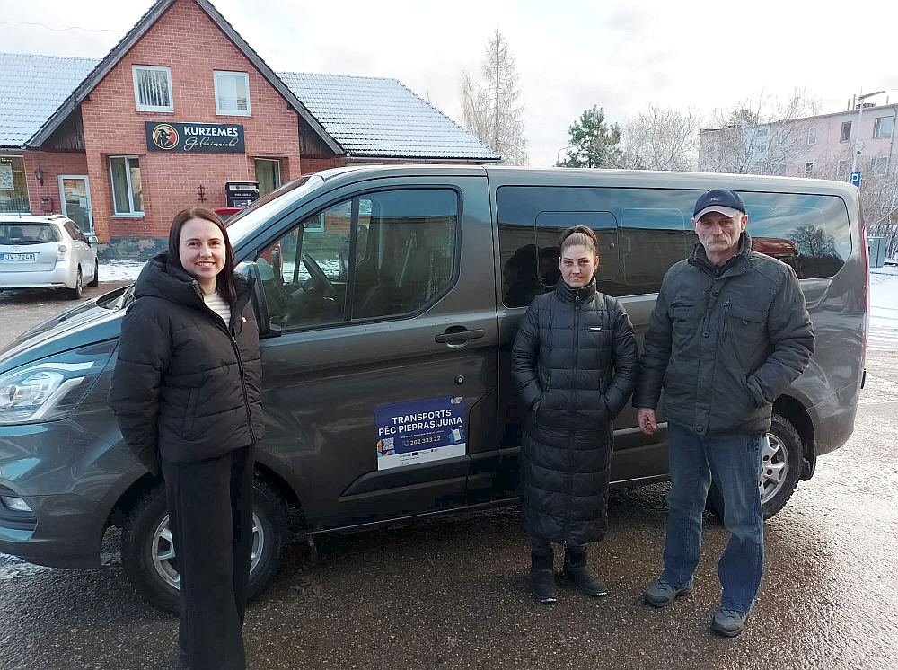 Kad pierod un iepazīst, visi ir apmierināti – par jauno pārvietošanās iespēju laukos saka pārvadātāju pārstāve Elīna Kramēna (no kreisās) un pasažieri no Vānes Kristīne Mitrofanova un Ivans Zvirs. Fonā – busiņš, ar kuru tiek pārvadāti pasažieri.