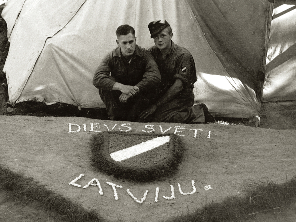 Internētie latviešu leģionāri pie pašdarināta rotājuma – latviešu leģiona vairodziņa. Ēkšes – Rennesletes nometne, 1945. gada
vasara.