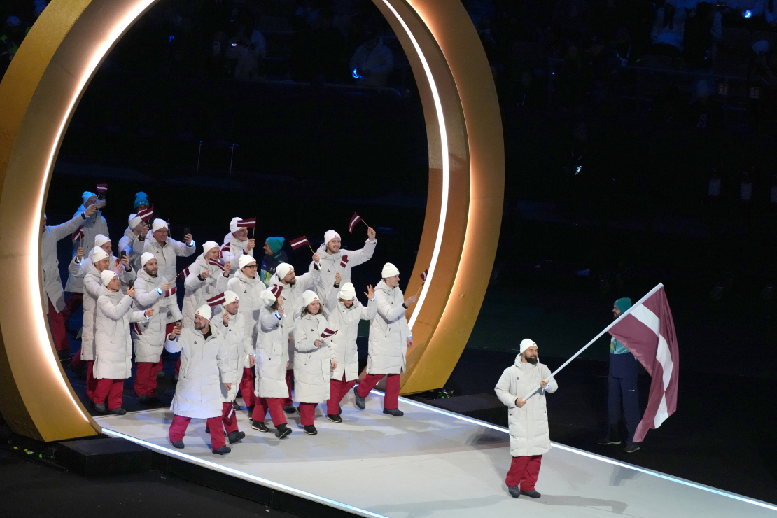 Latvijas karognesējs 2026. gada ziemas olimpiskajās spēlēs, hokejists Kaspars Daugaviņš (no labās) un Latvijas delegācijas sportisti 2026. gada Milānas un Kortīnas ziemas olimpisko spēļu atklāšanas ceremonijā "San Siro" stadionā Milānā, Itālijā.