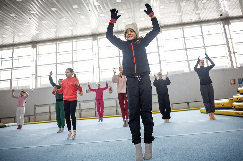 Kijivā un citās Ukrainas pilsētās ir elektroenerģijas un apkures pārtraukumi pēc Krievijas uzbrukumiem kritiskajai infrastruktūrai. Attēlā: skolas vingrošanas zālē gaisa temperatūra nepārsniedz +5 grādus, tāpēc meitenes vingrinājumus veic, uzvilkušas siltas zeķes, cimdus, ziemas cepures.