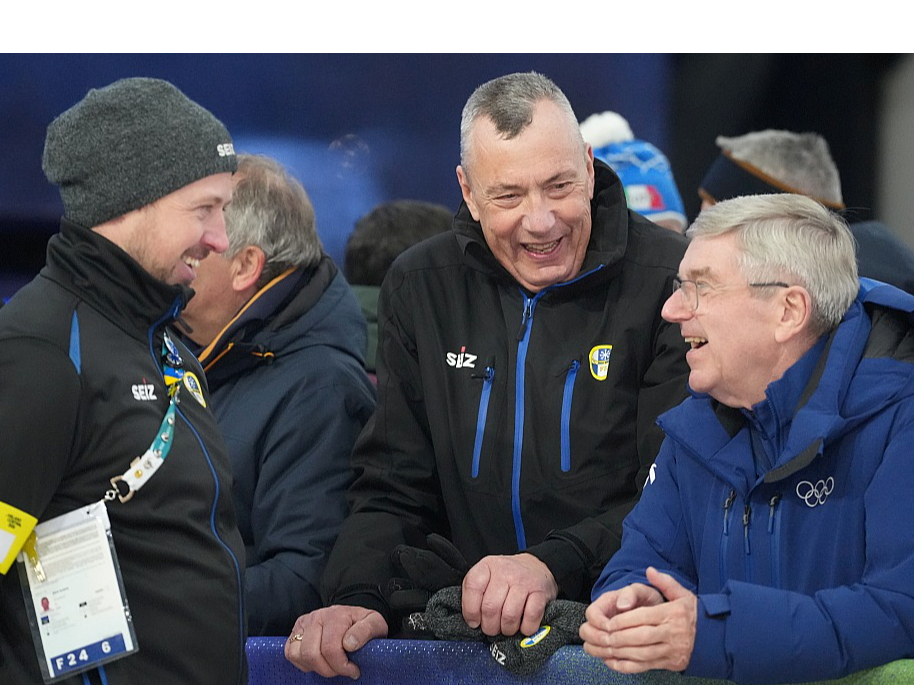 Bijušo Starptautiskās olimpiskās komitejas prezidentu Tomasu Bahu (no labās) izklaidē latvieši – Starptautiskās kamaniņu sporta federācijas prezidents Einars Fogelis un agrāk titulētais kamaniņnieks, šobrīd starptautiskās federācijas mākslīgās ledus trases tehniskais direktors Andris Šics.