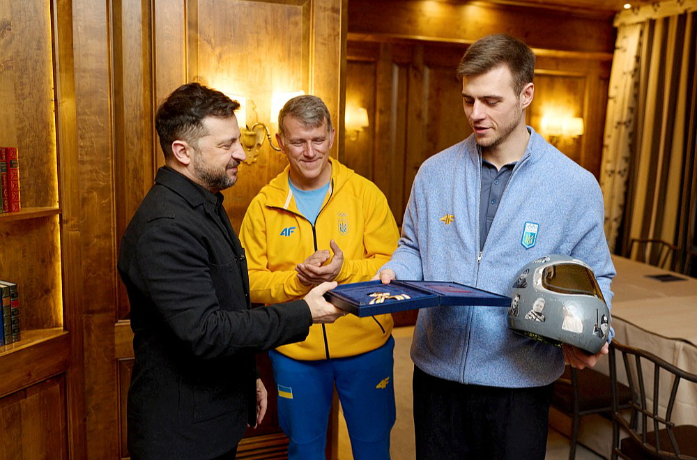 Ukrainas prezidents Volodimirs Zelenskis (no kreisās) Minhenes drošības konferencē tikās ar skeletonistu Vladislavu Heraskeviču, pasniedzot viņam Brīvības ordeni. Vidū tēvs un treneris Mihailo Heraskevičs.