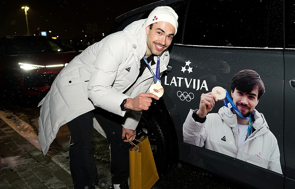 Olimpiskais medaļnieks Roberts Krūzbergs pozē pie mašīnas ar olimpiskā medaļnieka bildi uz tās. Šorttrekists atzīst, ka tik lielu uzmanību no apkārtējiem izbauda pirmo reizi dzīvē.