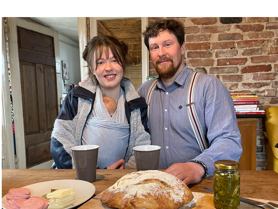 Ellena un Gunārs ar savu pirmdzimto lielajā istabā, kur uz brokastu galda
ir arī saimnieka cepta maize.