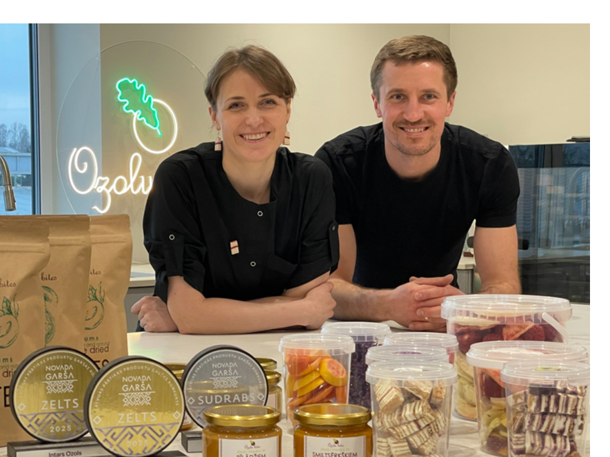 Marta un Intars Ozoli savā jaunajā ražotnē pie lielā darba galda, uz kura izlikts teju viss viņu ražojumu klāsts, kā arī “Novada garšas” konkursā iegūtās godalgas. Priekšplānā – gabaliņos sagrieztā medus kūka.