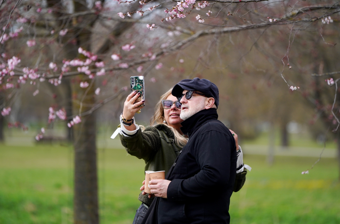 Cilvēki fotogrāfējas pie sakurām Uzvaras parkā.