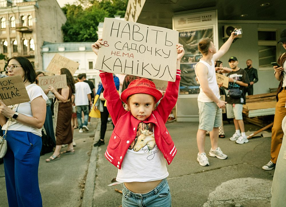 Simtiem ukraiņu vairākas dienas Kijivā piedalījās protesta akcijās pēc Ukrainas aizsardzības ministra Mihailo Fedorova atcelšanas no amata. Daudzi no protestētājiem pauda neapmierinātību ar reformu trūkumu armijā. Uz šīs protesta dalībnieces plakāta ukraiņu valodā rakstīts: "Pat bērnudārzā nav brīvlaika". Tas ir kā satīrisks sabiedrības pārmetums Ukrainas augstākajai vadībai par to, ka kara laikā nemitīgi tiek mainītas svarīgas amatpersonas, neļaujot tām pabeigt uzsāktās reformas. Plakāts arī simbolizē Ukrainas sabiedrības un jo īpaši jaunās paaudzes nogurumu no iekšējām politiskajām cīņām un pieprasījumu pēc stabilitātes un reālām reformām frontē, kur brīvdienu nav nevienam.