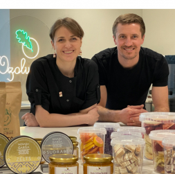 Marta un Intars Ozoli savā jaunajā ražotnē pie lielā darba galda, uz kura izlikts teju viss viņu ražojumu klāsts, kā arī “Novada garšas” konkursā iegūtās godalgas. Priekšplānā – gabaliņos sagrieztā medus kūka.