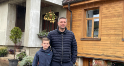 Saimnieks Ivars Grantiņš ar dēlu Ernestu mājas pagalmā, kur labi redzams, kā senākā daļa savienota ar no jauna uzbūvēto nodegušā apjoma
vietā.