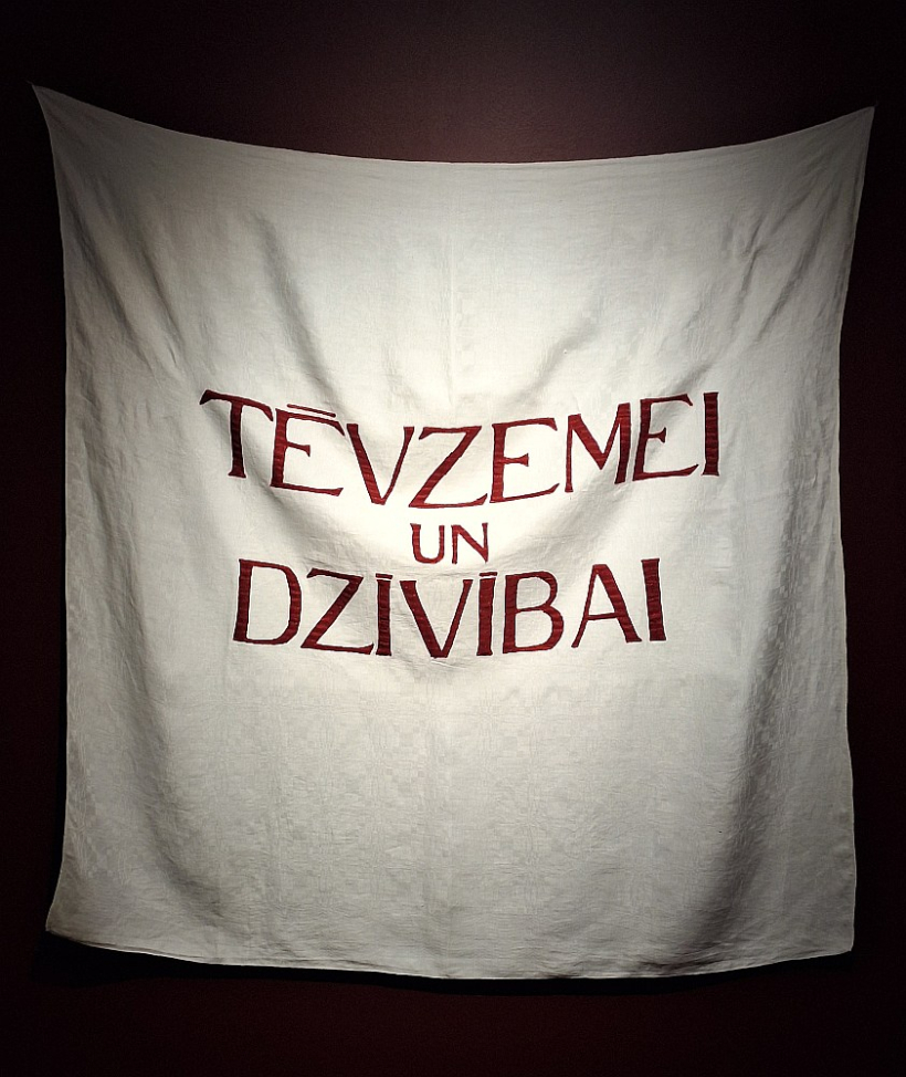 Laura Dzērve. "Tēvzemei un dzīvībai". 2025, tekstila aplikācija, 140 x 140 cm. Māksliniece teic: "Mēs vienmēr esam tiekušies pēc brīvības, bet vai protam dzīvot brīvā valstī? Vai, baudot šo brīvību, spējam izvēlēties atbildīgi?"